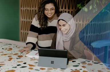 Dos mujeres sonríen ante un ordenador para ilustrar cómo pagar a los empleados internacionales
