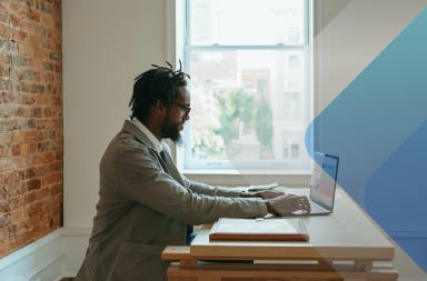 Un hombre utiliza una computadora portátil junto a una ventana para ilustrar un artículo sobre la gestión del personal distribuido